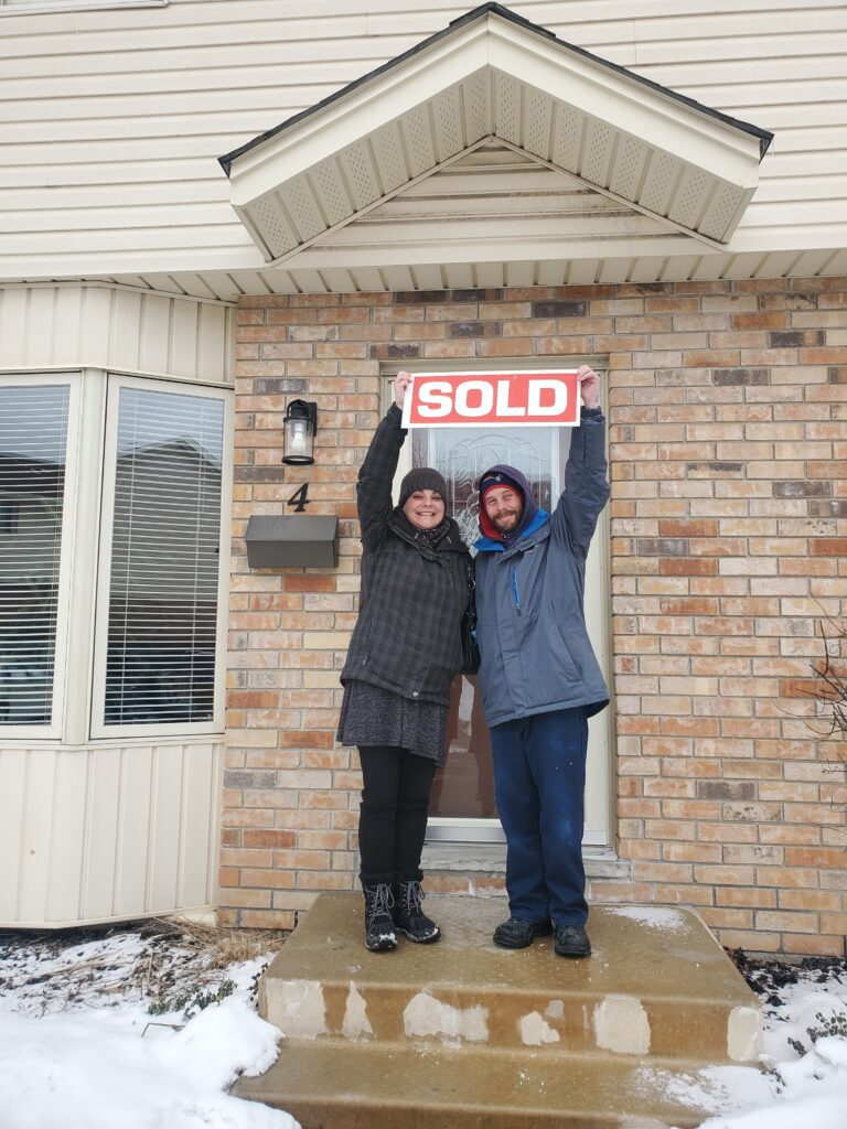 Couple with sold sign in front of their home purchased with Nicole McKenzie, Taking you Home