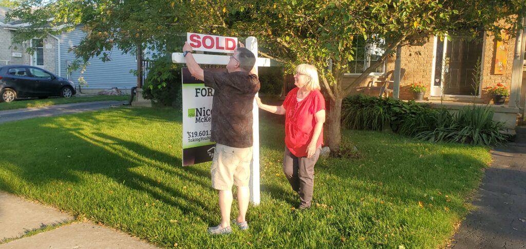 Couple with sold sign in front of their home sold with Nicole McKenzie, Taking you Home