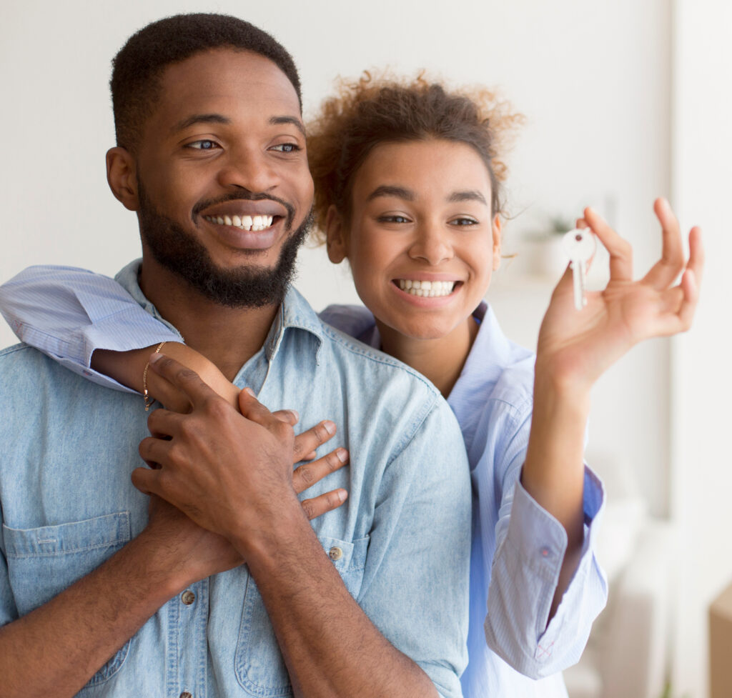 Happy Black Couple Hugging Showing Key Standing In New Home.