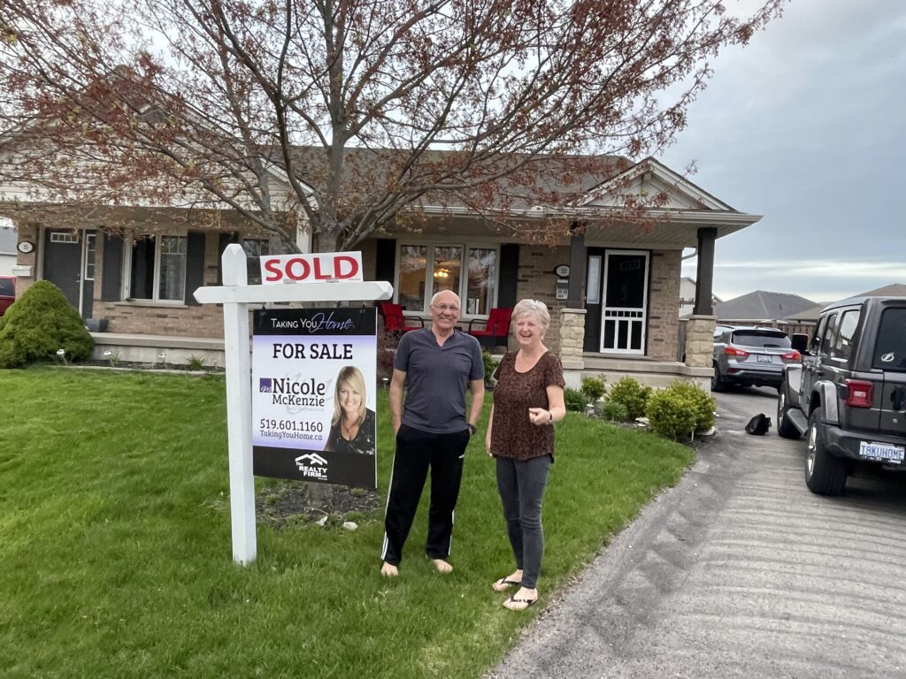 Retired couple with sold sign in front of their home sold with Nicole McKenzie, Taking you Home